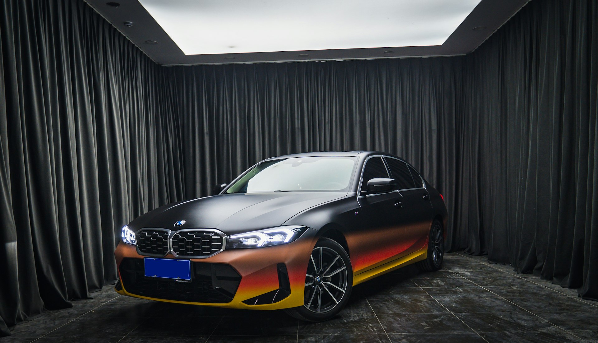 a black car with orange and yellow stripes parked in front of a black curtain